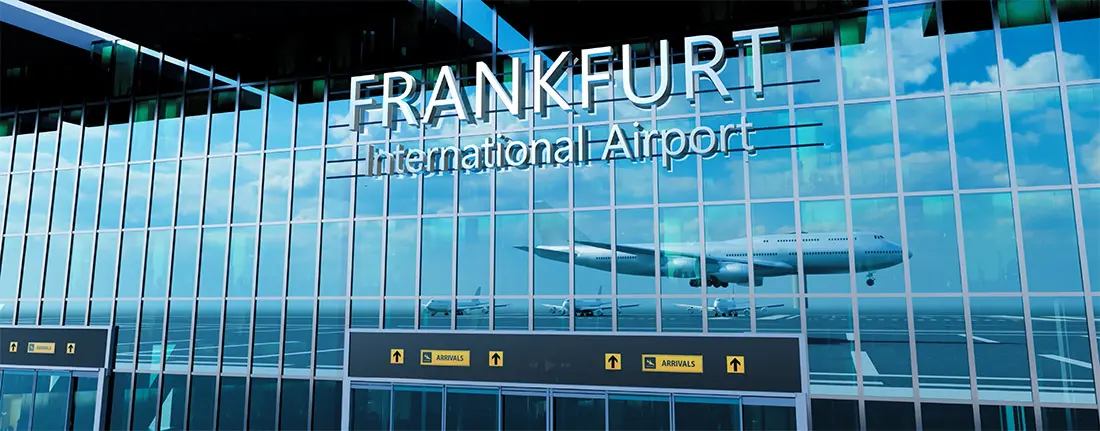 Glasfassade des Frankfurt International Airport mit großem Schriftzug und Spiegelungen von Flugzeugen auf dem Vorfeld. Unterhalb der Fensterfront befinden sich Eingänge und Wegweiser für ankommende Passagiere.
