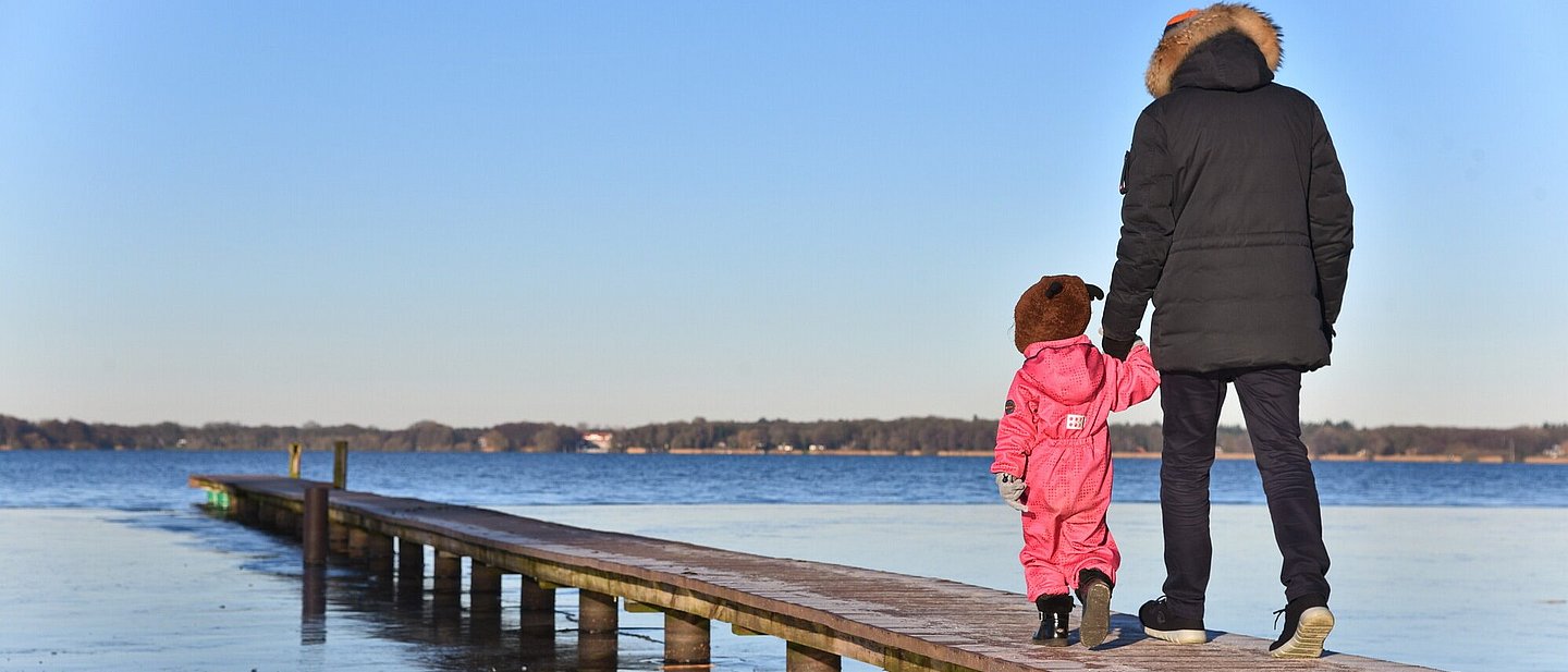 Ein Vater mit seinem Kind Hand in Hand auf einem Steg über Wasser