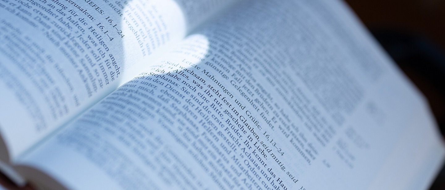 Ein kreisrunder Lichtschein scheint auf eine aufgeschlagene Bibel und zeichnet ein Herz. Im Fokus ist die Jahreslosung 2024 zu erkennen.