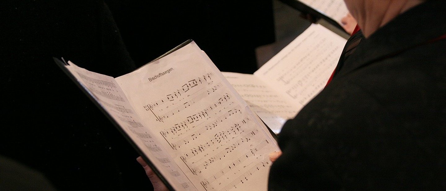 Man blickt auf ein Notenblatt über die Schulter einer Sängerin hinweg