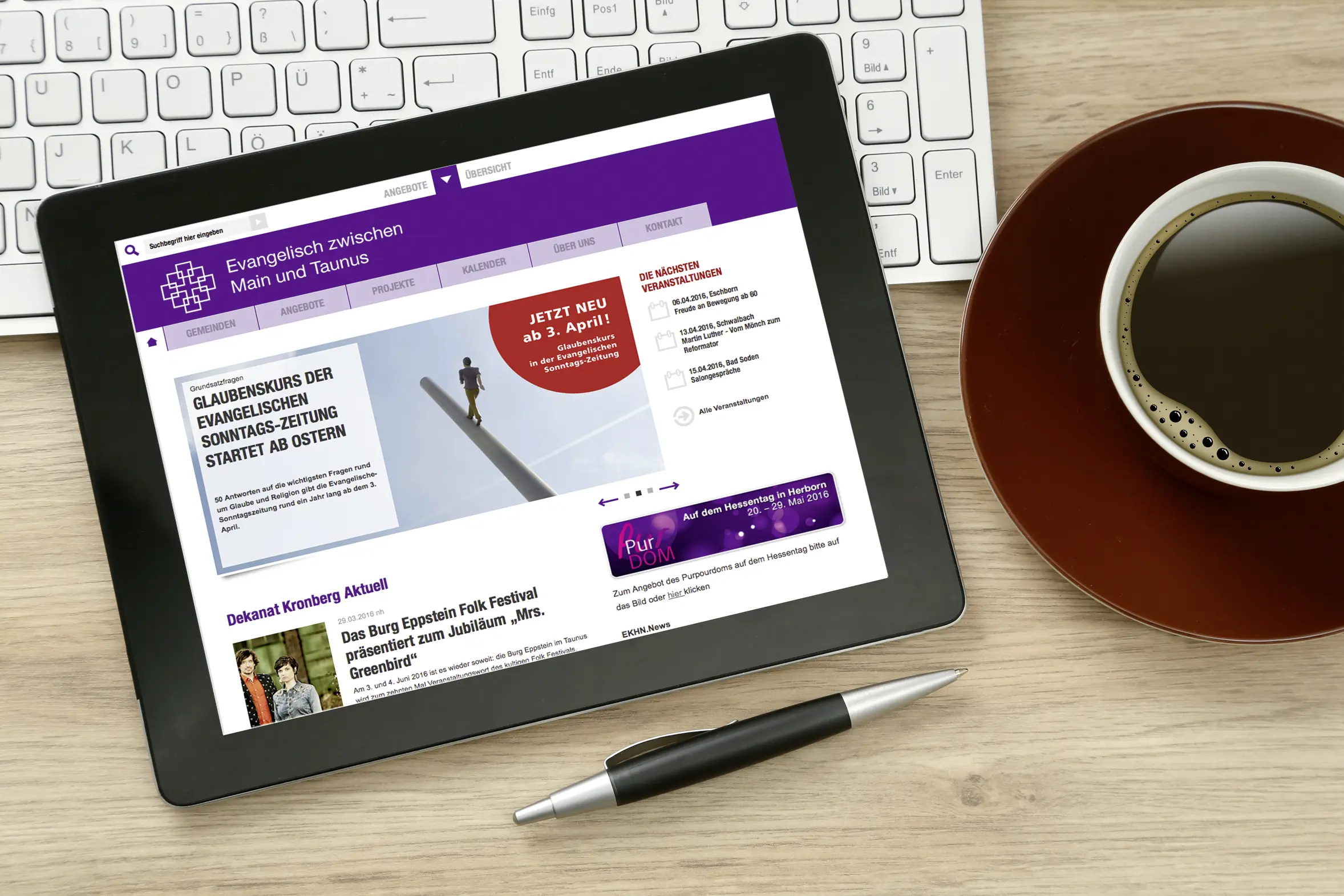 Auf einem Tisch liegen neben einer Tastatur, einem Stift und einer Kaffeetasse ein Tablet, auf dem die Website des Dekanats Kronberg zu sehen ist
