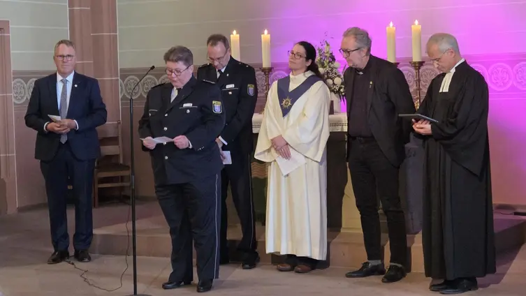 Sechs Personen stehen vor dem Altar und beten. Zwei tragen eine Polizeiuniform, zwei tragen Talare.