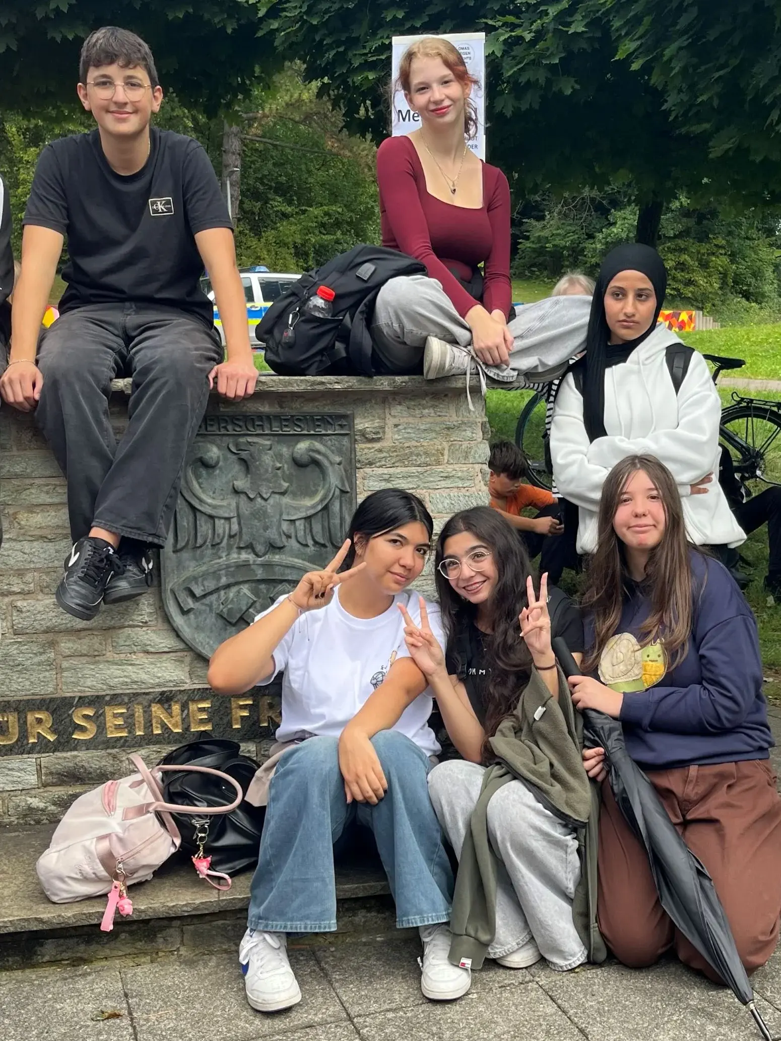 Fünf Schülerinnen und ein Schüler sitzen draußen auf einer Mauer und machen das Peacezeichen, sie setzen sich gegen die Abschiebung ihrer Mitschüler ein