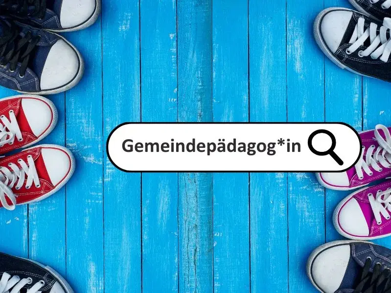 Ein Suchfeld mit dem Wort "Gemeindepädagog*in" und dem Ikon einer Lupe vor einem Hintergrund aus blau gestrichenen Holzbalken. Am rechten Bildrand sind die Anschnitte von Sneakers zu sehen. 