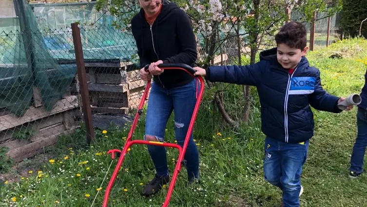 KiTa-Kinder beim Rasenmähen im eigenen Garten.