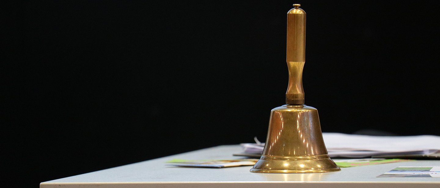 Auf einem Tisch steht eine messingfarbene Vorstandsglocke, die der Sitzungsleitung der Synode dient. 