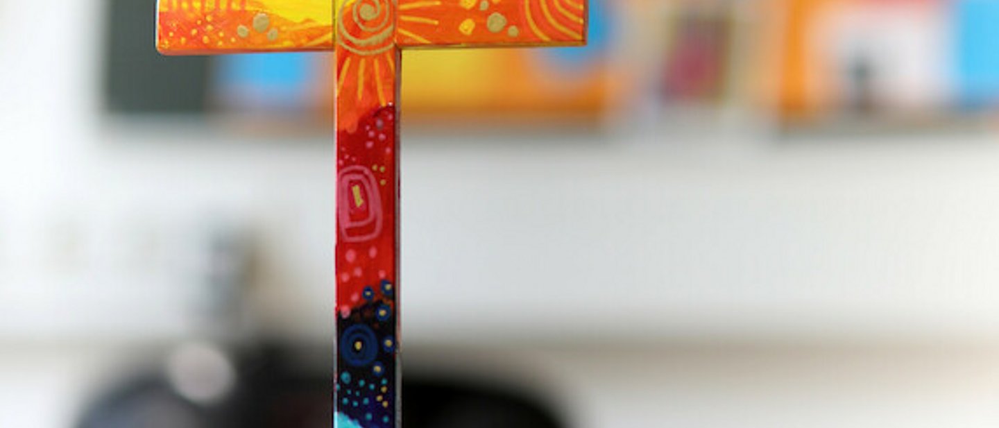 buntes Holzkreuz auf Tuch auf einem Tisch.