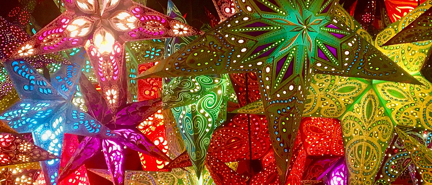 Viele Bunte beleuchtete Weihnachtssterne aus Papier. Verschiedene dekorative Muster wurden in die Sterne gestanzt oder geschnitten.