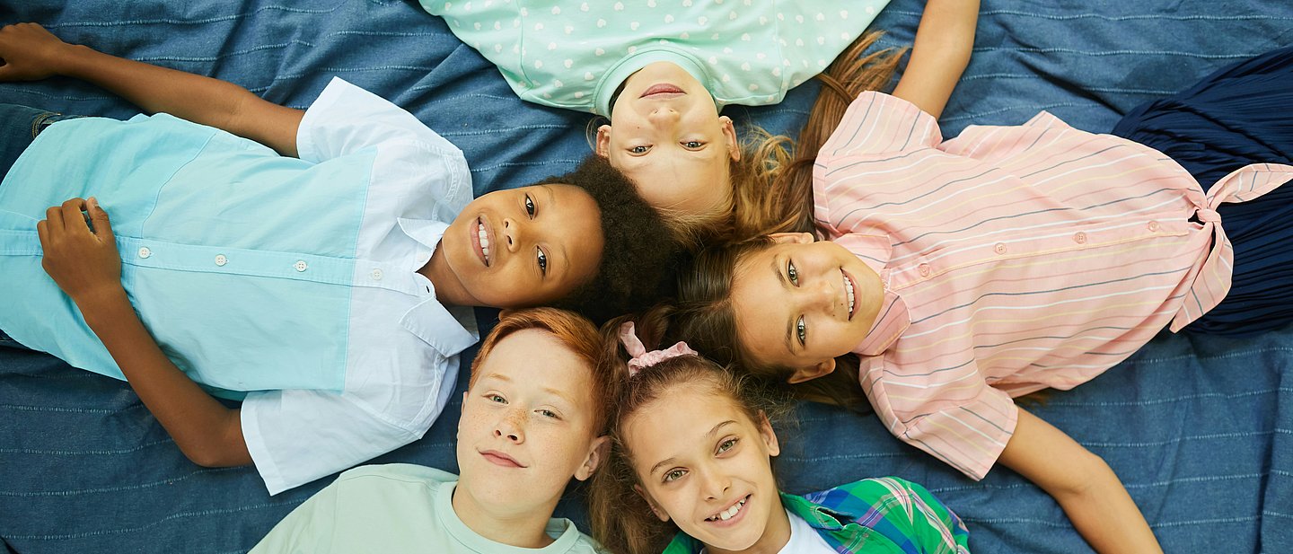 Fünf Jugendliche liegen sternenförmig auf dem Boden und schauen nach oben.