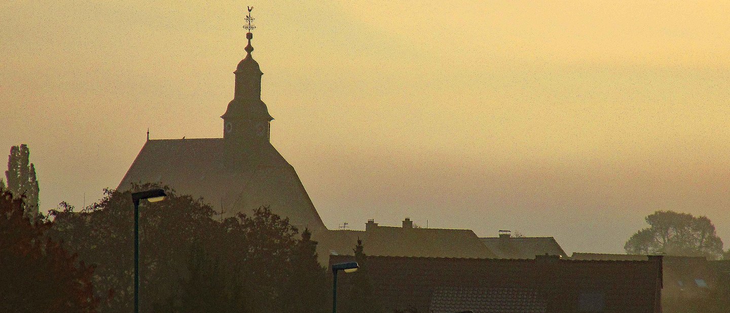 Die Silhouette Burgholzhausens mit der evangelischen Kirche im Nebel von Friedrichsdorf aus gesehen.