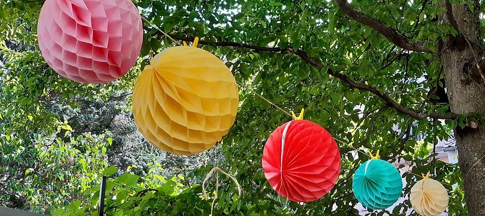 Bunte Lampions aus Papier hängen auf einer Wäschleine in einem Baum