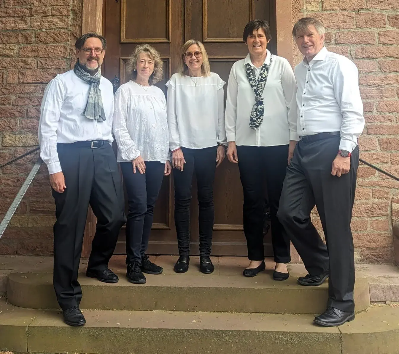 Zwei Sängerinnen, zwei Sänger und eine Pianistin vom Ensemble NahDran stehen vor dem Eingang der Ev. Kirche Liederbach.