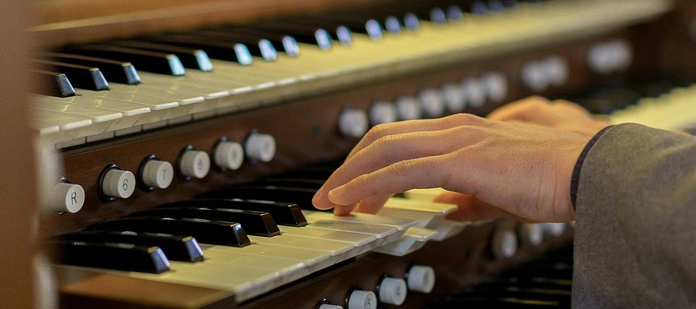 Nahaufnahme eine Orgelklaviatur mit 2 Händen, die darauf spielen