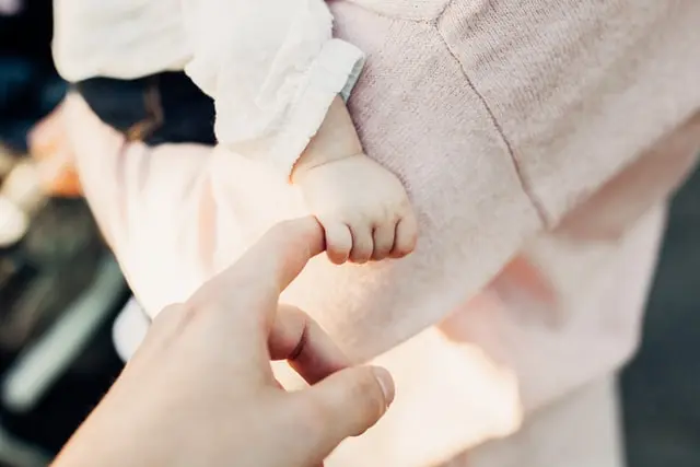 Ein Baby auf dem Arm der Mutter greift einen Finger
