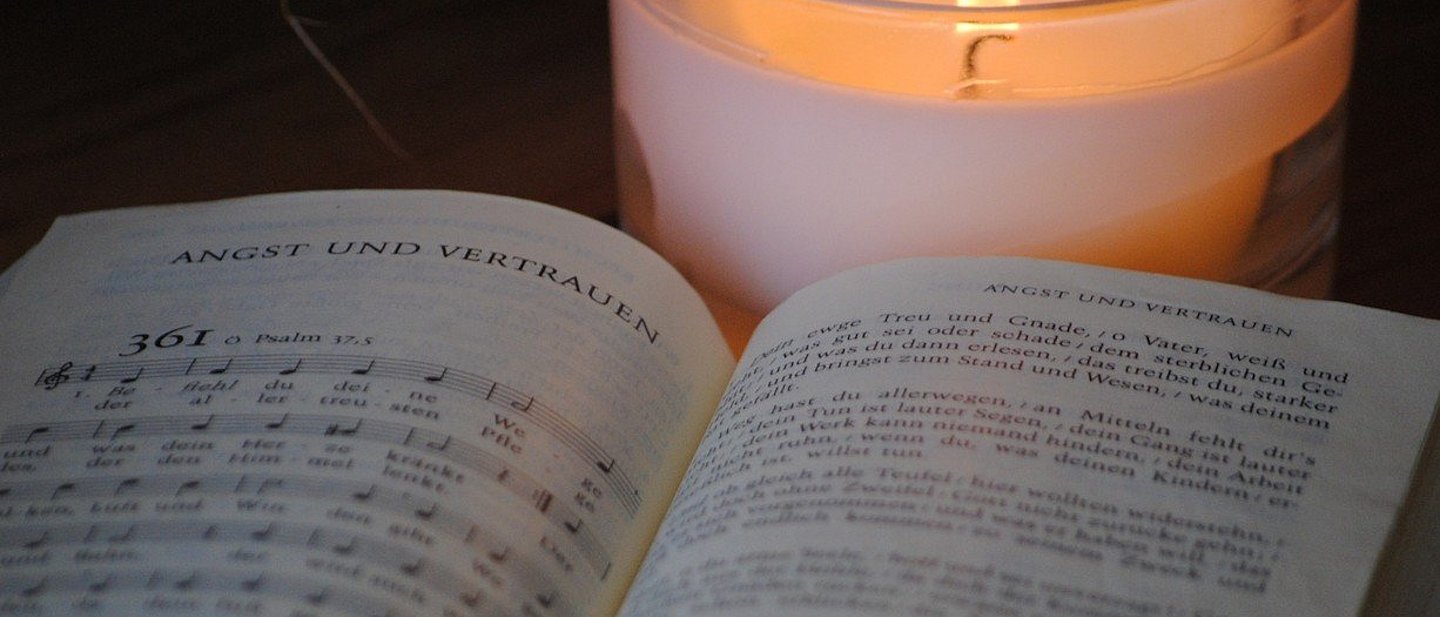 Aufgeschlagenes Evangelisches Gesangbuch mit Nummer 361; dahinter brennt eine weiße Kerze.