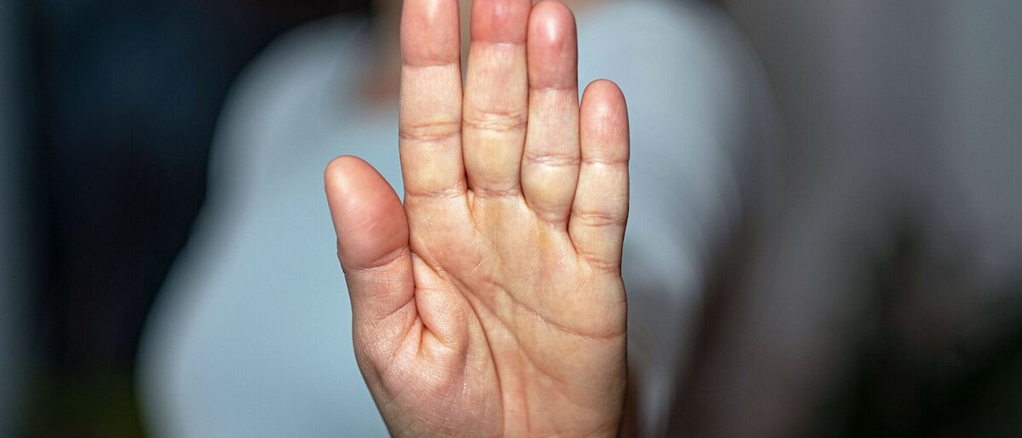 Eine Frau streckt ihre Handfläche aus und in die Kamera. Der Fokus liegt auf der Handfläche, der Rest ist verschwommen.