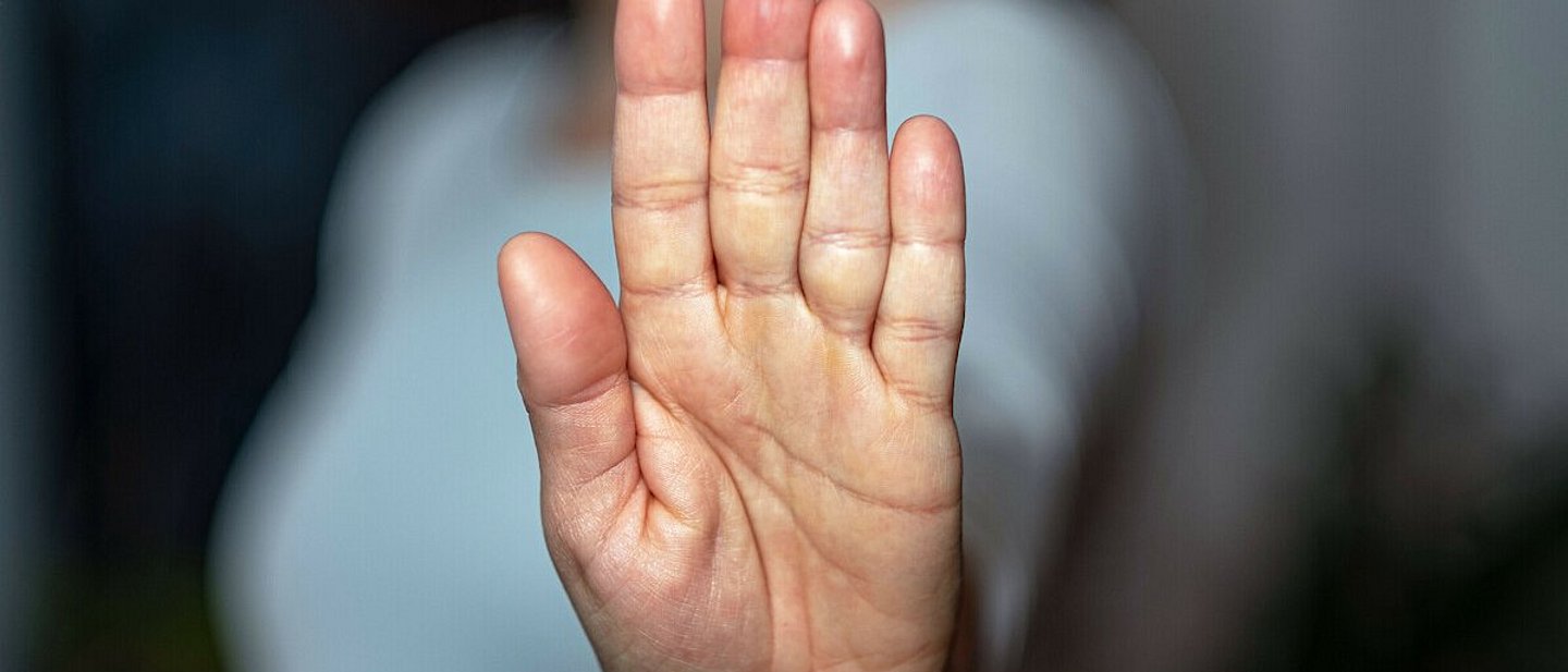 Eine Frau streckt ihre Handfläche aus und in die Kamera. Der Fokus liegt auf der Handfläche, der Rest ist verschwommen.