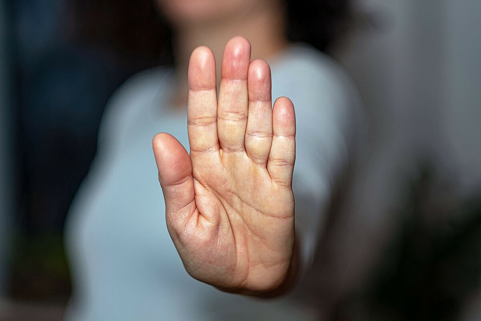 Eine Frau streckt ihre Handfläche aus und in die Kamera. Der Fokus liegt auf der Handfläche, der Rest ist verschwommen.