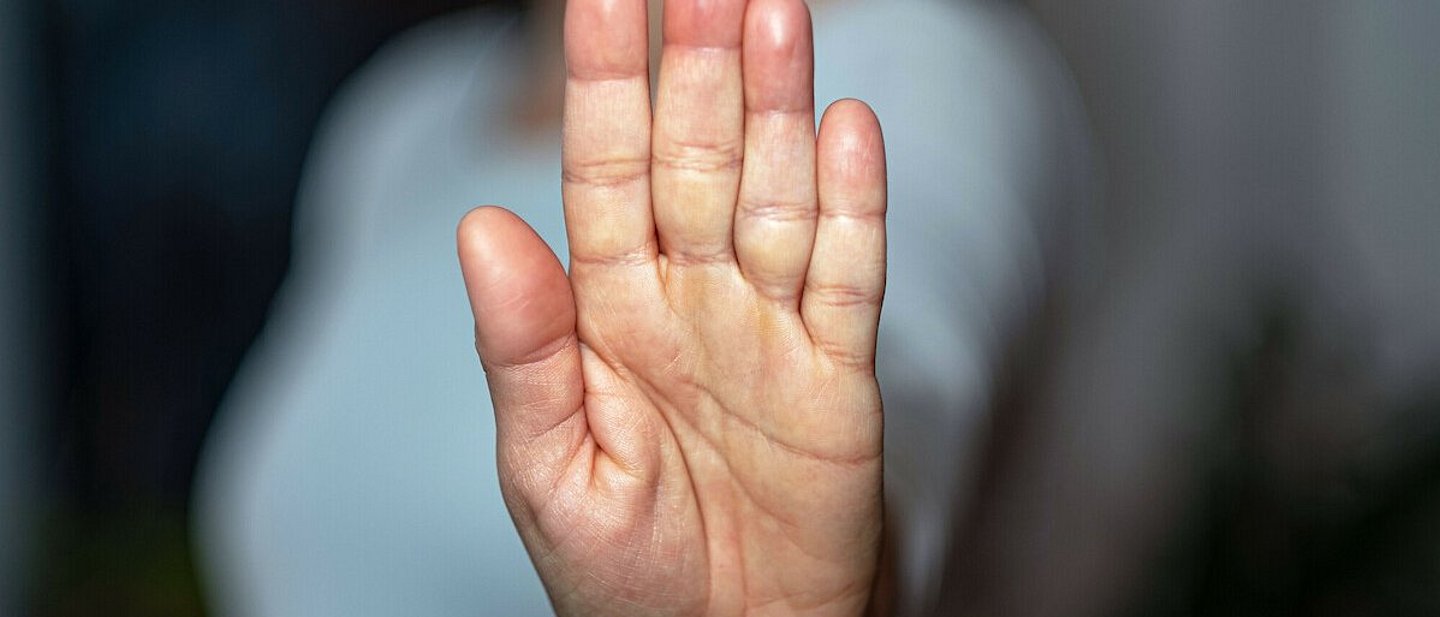 Eine Frau streckt ihre Handfläche aus und in die Kamera. Der Fokus liegt auf der Handfläche, der Rest ist verschwommen.