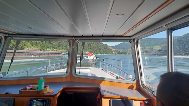Blick vom Steuerstand des Polizeiboots über den Bug auf den Fluss. Im Hintergrund Schiffe und die Berglandschaft am Rhein.