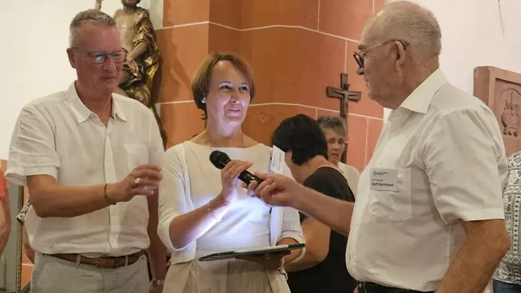 Dekan Guth, Dekanin Hamrich und Präses Hartmann, alle in weißen Hemden bzw. weißer Bluse, im Altarraum der Niddaer Stadtkirche, reichen ein Mikrofon weiter.