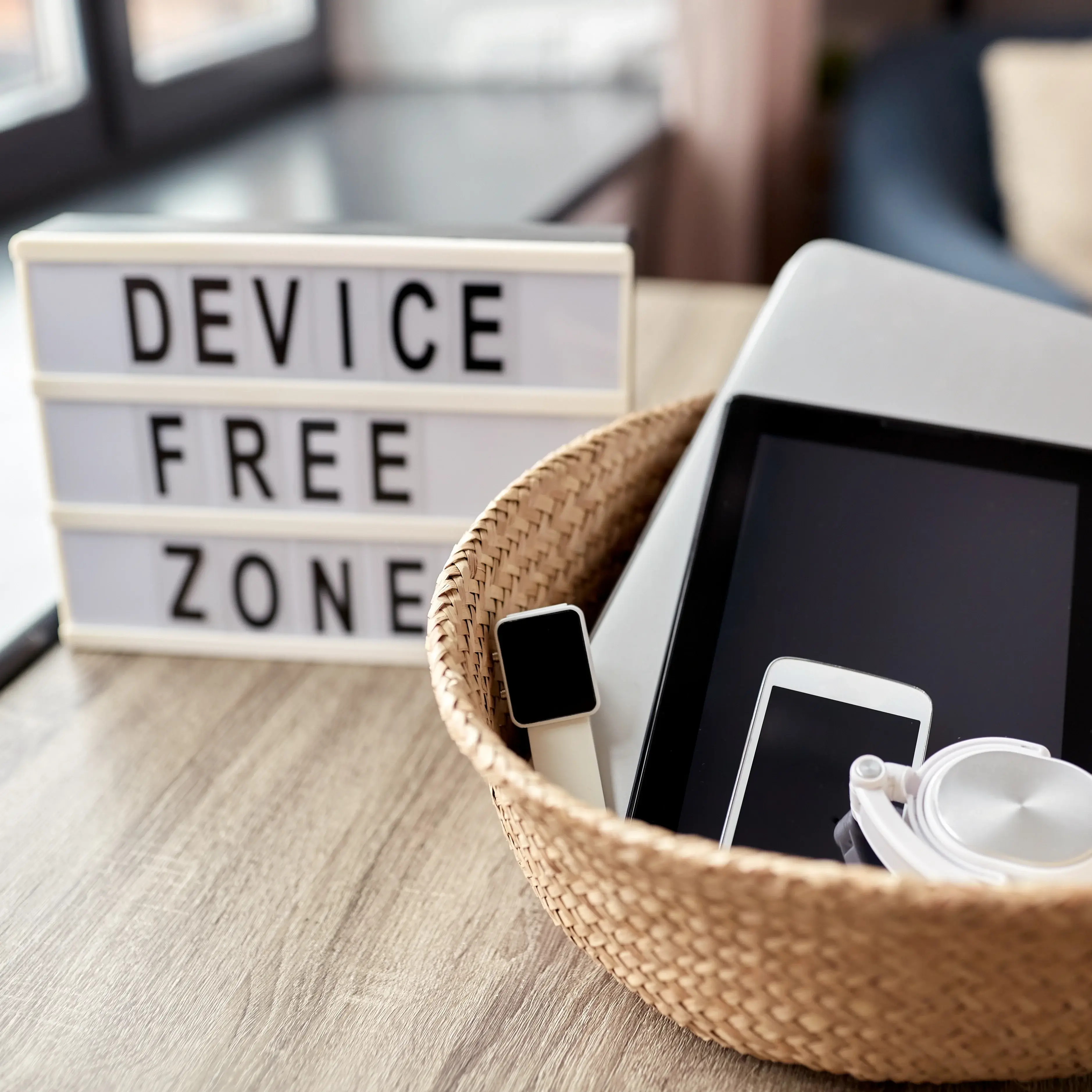 In einem Korb liegen Tablett, Kopfhörer, Handy und anderes. Dahinter eine Leuchtbox mit den Worten "Device free Zone" 