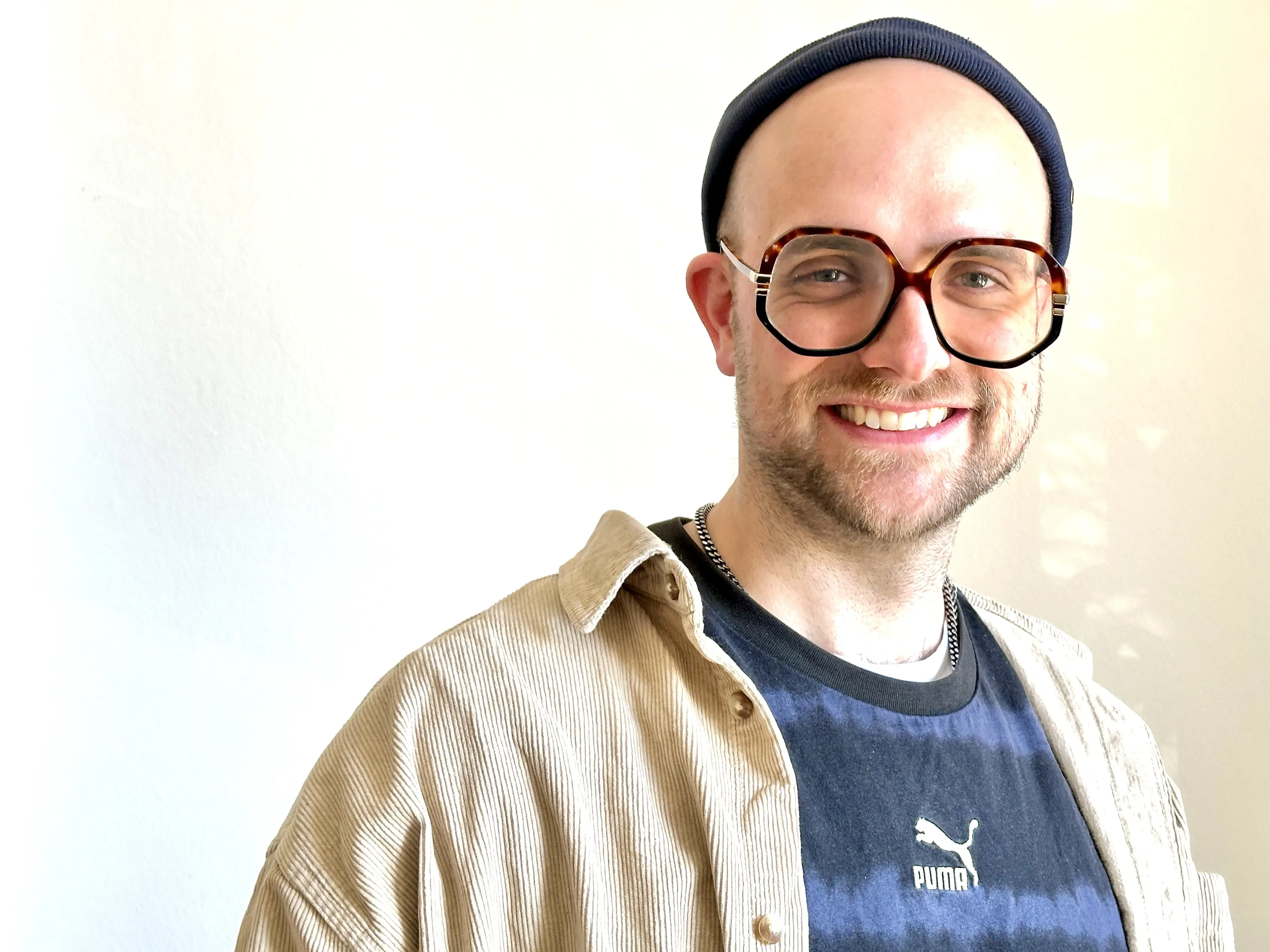 Pfarrer Dr. Adrian Schleifenbaum Das Bild zeigt einen jüngeren Mann, der leger gekleidet ist, ein große, modische Brille trägt.