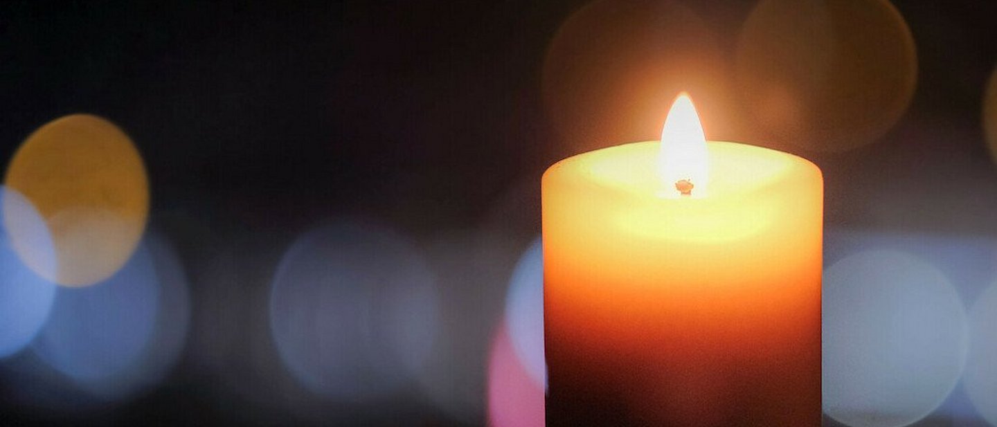 Kerze zum Gedenktag der Coronatoten am 18.4.2021. In der Bildmitte eine brennende Kerze mit dahinterliegenden Bokeh-Effekten in der Unschärfe.