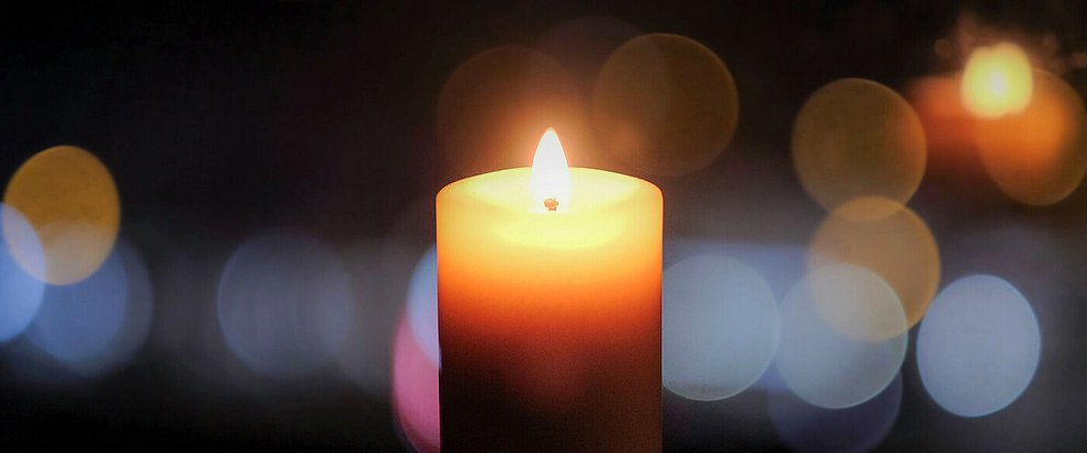 Kerze zum Gedenktag der Coronatoten am 18.4.2021. In der Bildmitte eine brennende Kerze mit dahinterliegenden Bokeh-Effekten in der Unschärfe.