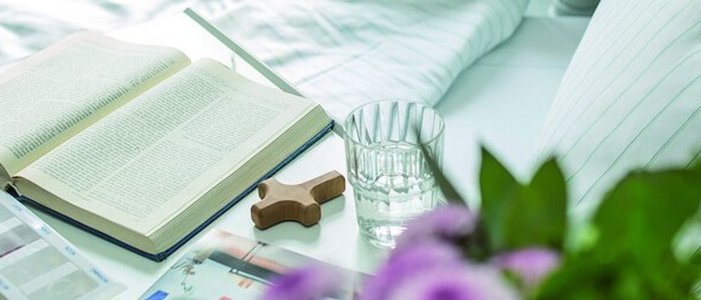 Ein Kreuz und eine aufgeschlagene Bibel liegen neben Medikamenten auf einem Krankenbett-Tisch.