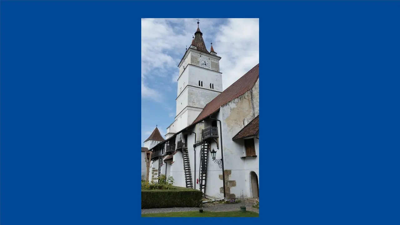 Im Hintergrund ist ein weißer Kirchturm zu sehen. Im Vordergrund ist der Kirchhof und ein Wohngebäude auf dem Kirchengelände.