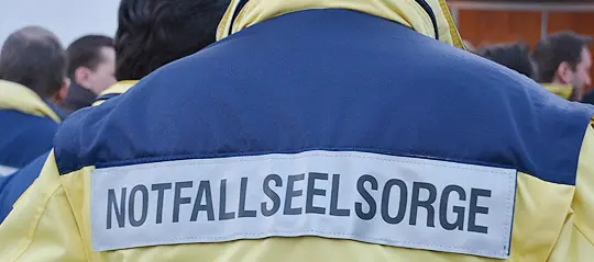 Der Rücken einer Person einer Person ist zu sehen. Auf ihrer Jacke steht "Notfallseelsorge".