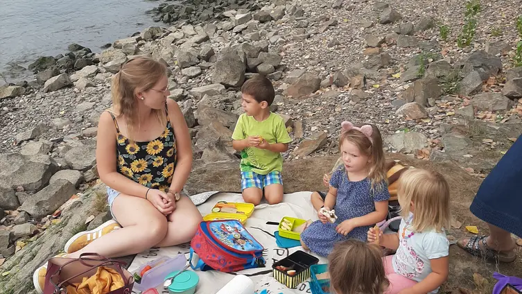 Auf dem Foto sieht man einige Kinder der Kindertagesstätte "Haus des Kindes" am Rhein picknicken.