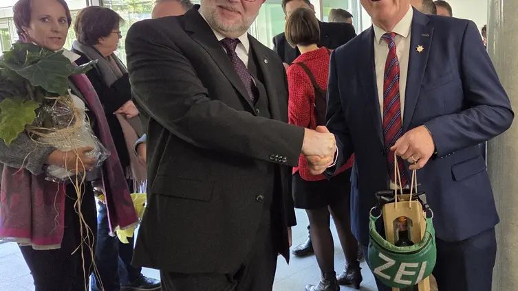 Die beiden Männer geben sich die Hand. Im Hintergrund stehen Festgäste beim Epmpfang  herum.