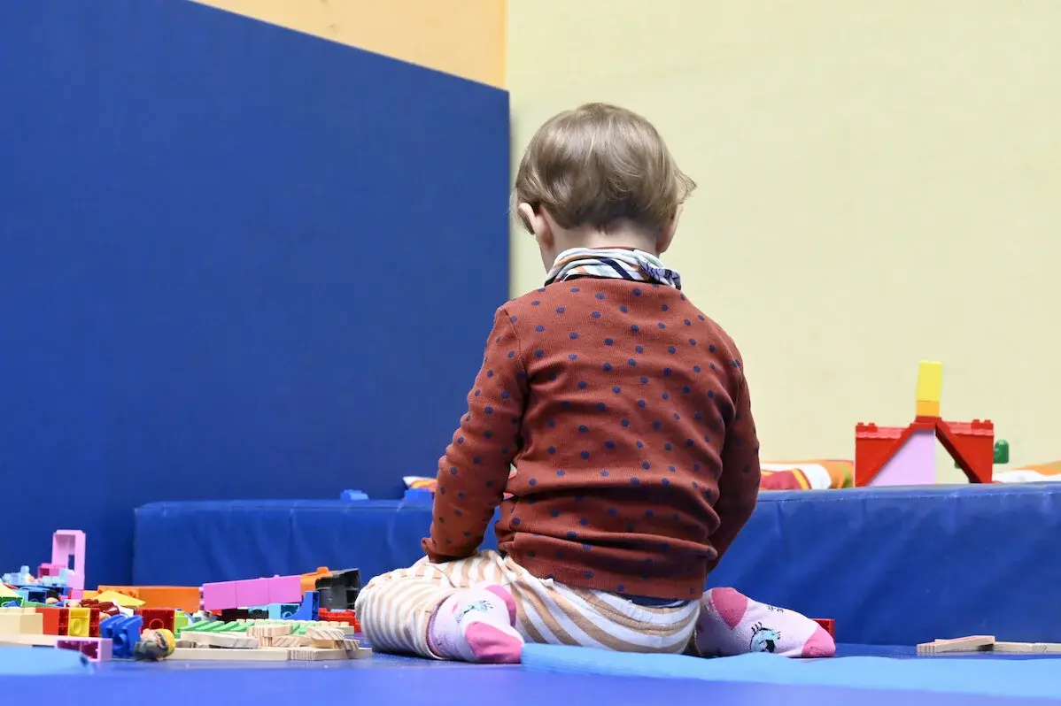 Kirche Kunterbunt – Kirche für Kinder und Erwachsene. Ein Kleinkind kniet mit dem Rücken zur Kamera auf einem blauen Tuch auf dem Fußboden und spielt mit Legosteinen.