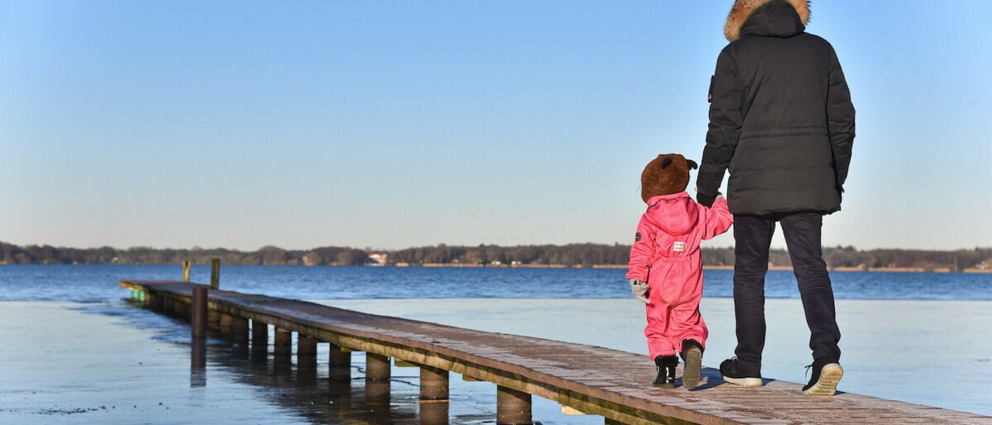 Ein Vater mit seinem Kind Hand in Hand auf einem Steg über Wasser