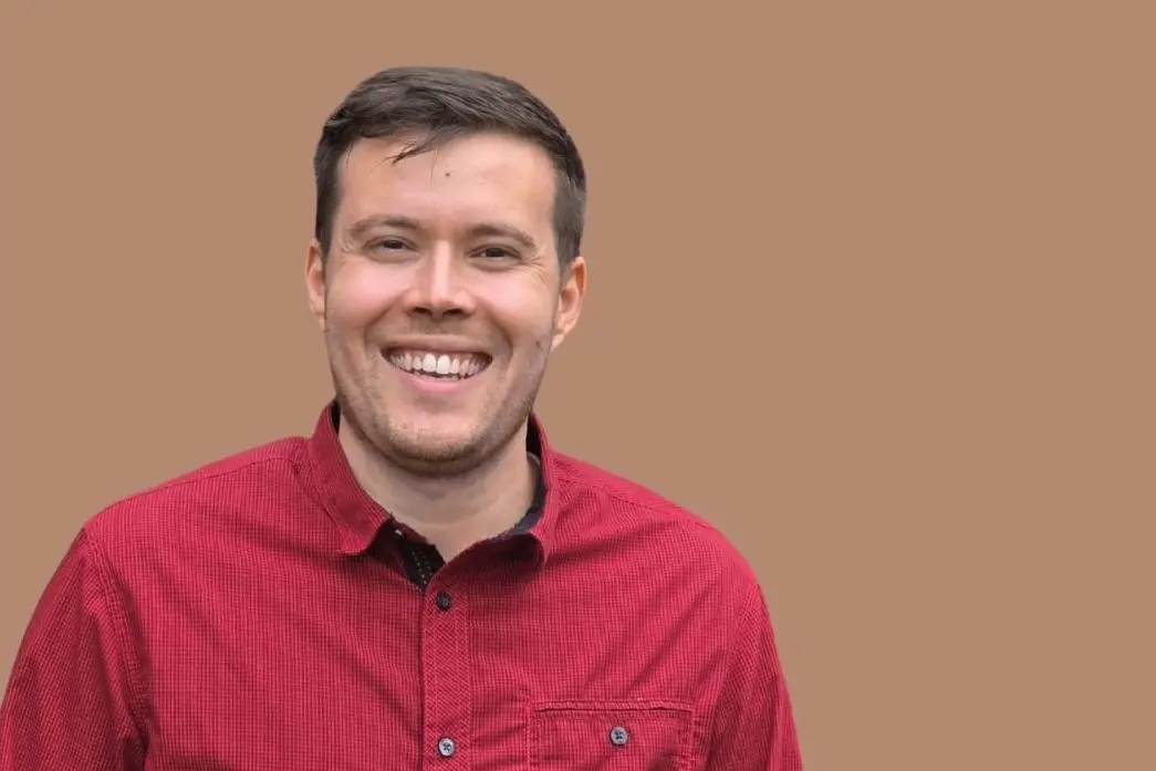 Florian Wachter, junger Mann mit kurzen dunklen Haaren und in einem roten Hemd lacht freundlich in die Kamera.
