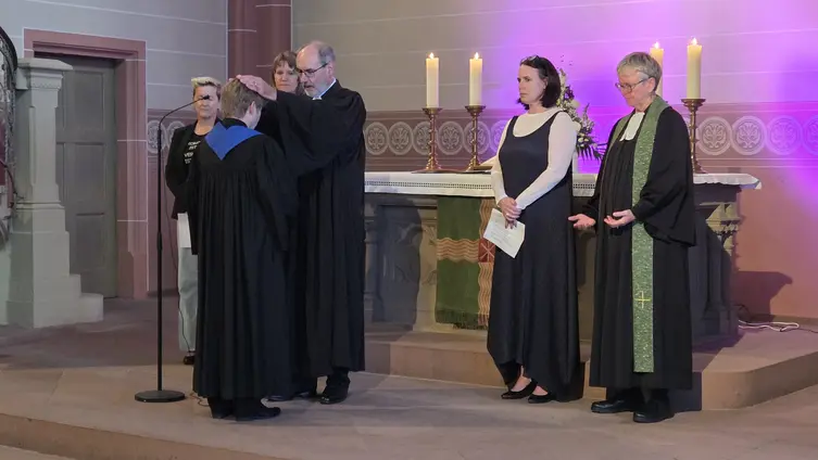 Vor dem Altar erhebt der Propst die Hände über der Pfarrerin. Vier Personen stehen als zeugen daneben.
