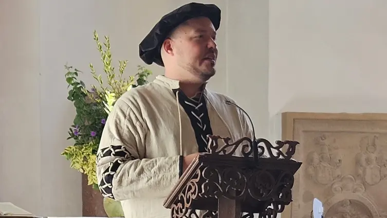 Jan-Philipp Repp in historischem Kostüm mit Kappe vor einem Stehpult in der Stadtkirche Nidda.