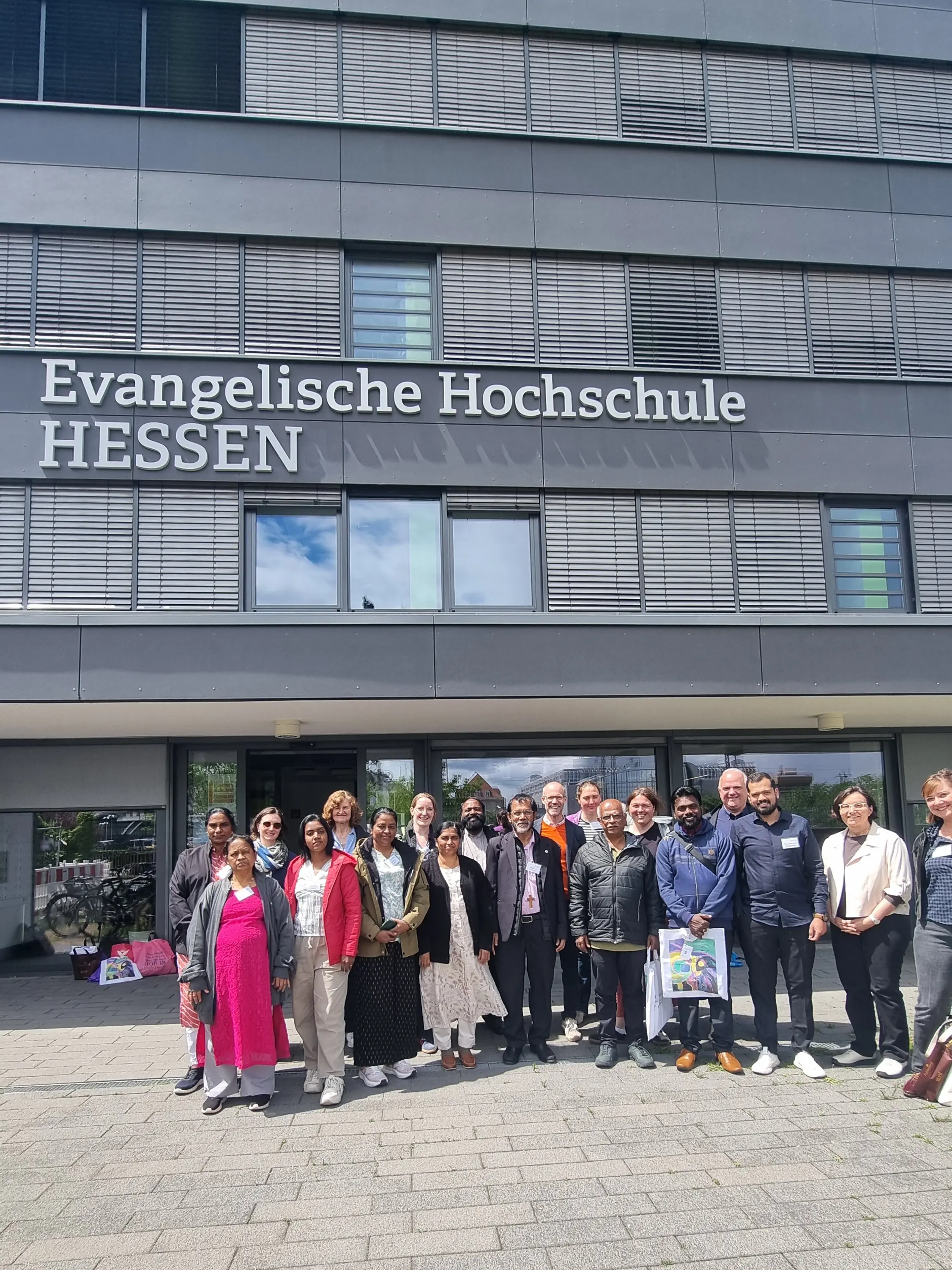 Große Menschengruppe steht vor einem großen Gebäude, das die Aufschrift Evangelische Hochschule Hessen trägt.