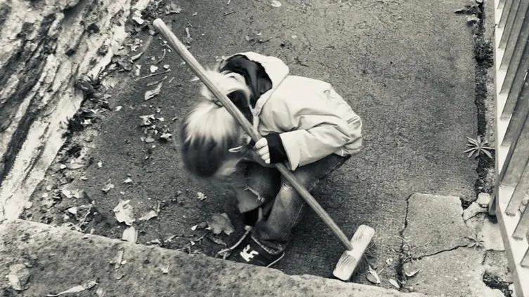 Das schwarz-weiß Foto zeigt 1 KiTa - Kind bei der "Hausmeister" - Arbeit vor der KiTa.