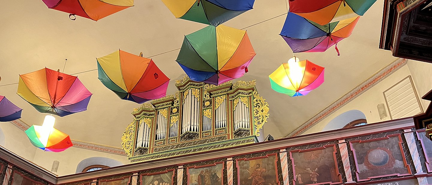 Blick in die Kirche St. Nikolai in Altenstadt, man sieht Orgelpfeifen und von der Decke hängend bunte Regenschirme