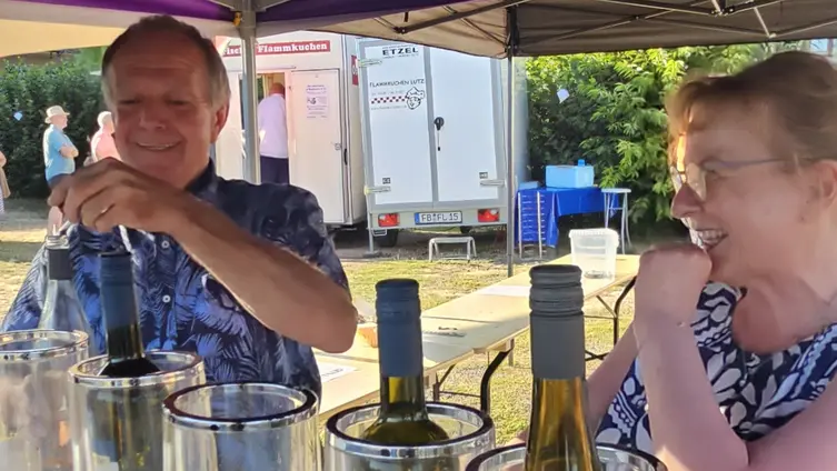 Klaus und Christine Ostheim, vor sich Weinkühler mit Flaschen, im Hintergrund sieht man Menschen und den Flammkuchenwagen.