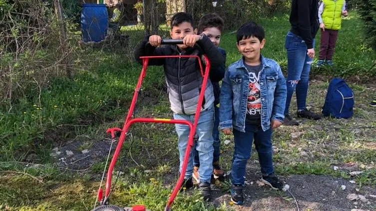 KiTa-Kinder beim Rasenmähen im eigenen Garten.