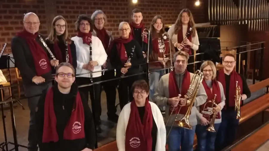Auf der Empore der Kirche stehen die Mitglieder des Posaunenchors mit ihren Instrumenten. Sie tragen einen roten Schal.