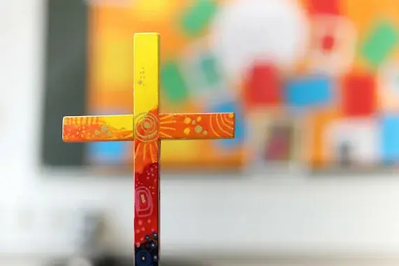 buntes Holzkreuz auf Tuch auf einem Tisch.