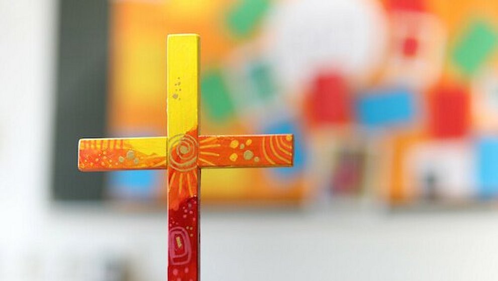 buntes Holzkreuz auf Tuch auf einem Tisch.