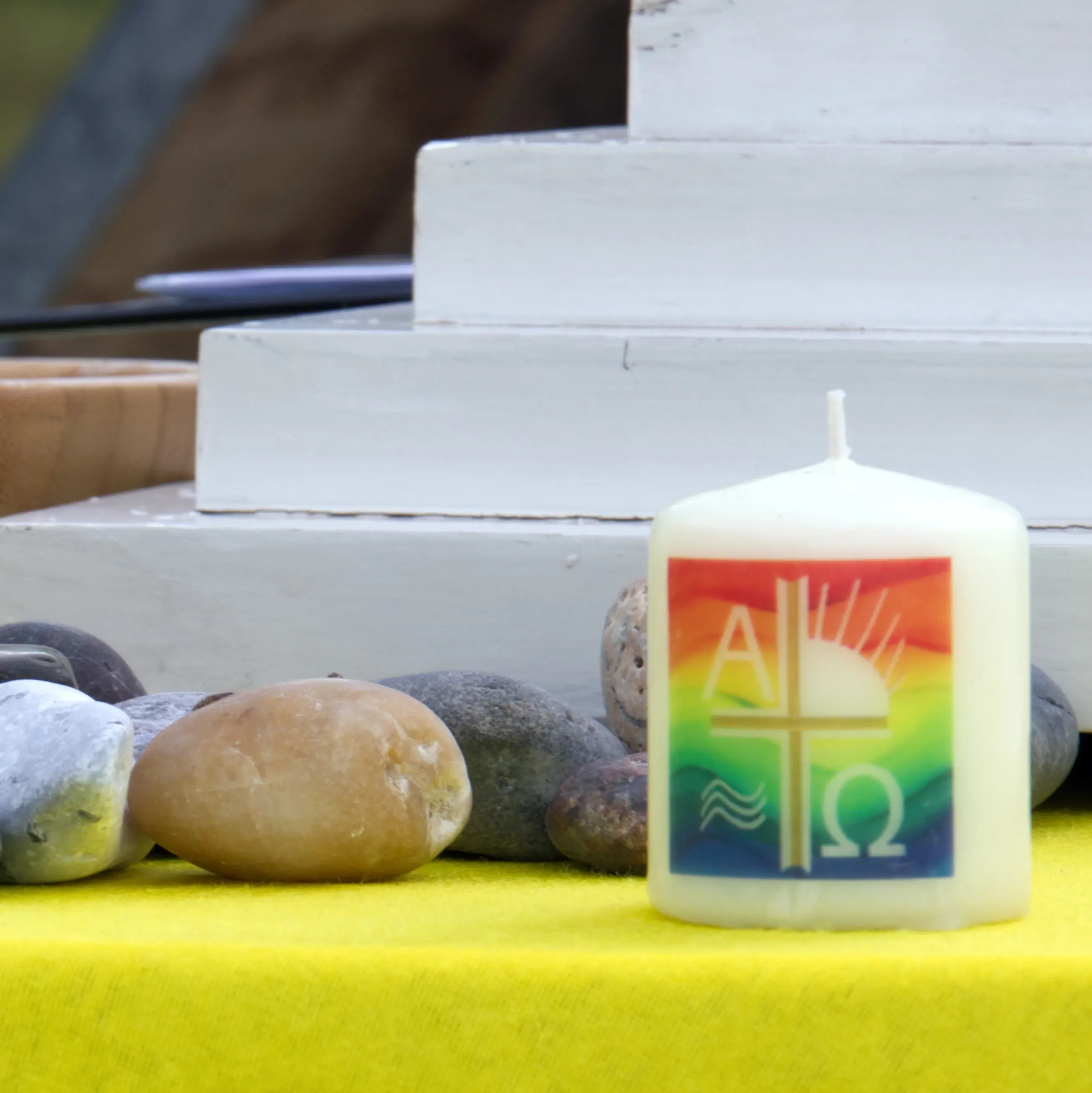 eine kleine Taufkerze auf einem Altar, daneben liegen Steine