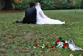 Brautpaar sitzend auf einer Wiese, von hinten; davor Schuhe