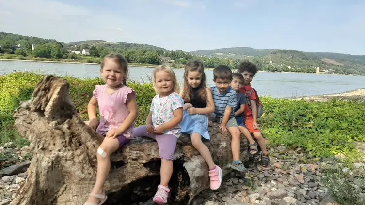 Das Foto zeigt Kinder, die auf einem angeschwemmten Baumstamm am Rheinufer sitzen.